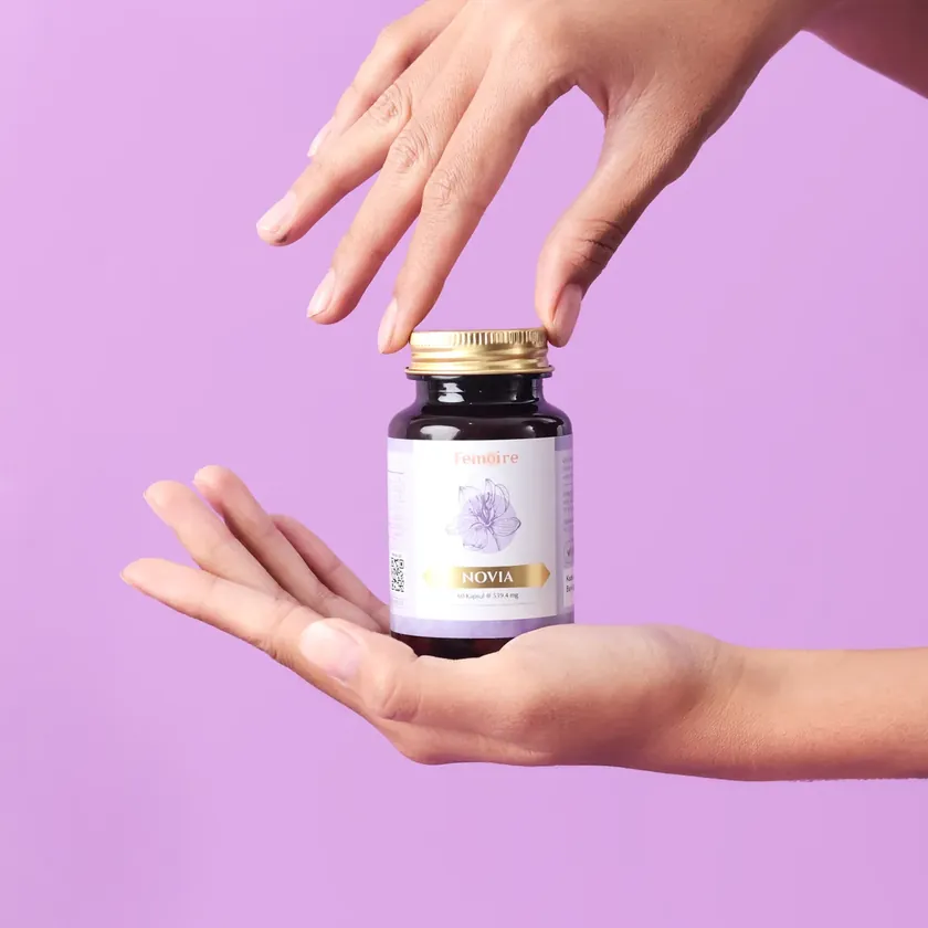 Tangan memegang botol NOVIA di latar ungu